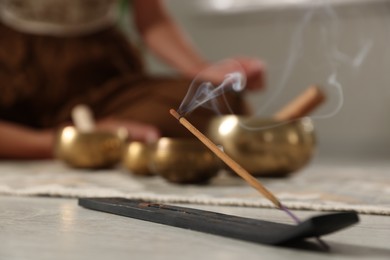 Photo of Incense stick smoldering in holder on floor indoors, selective focus