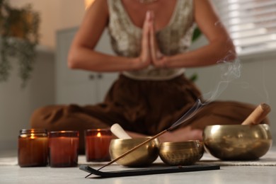 Young woman practicing yoga on floor indoors, focus on smoldering incense stick and tibetan singing bowls