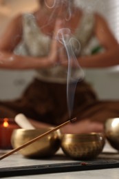 Young woman practicing yoga on floor indoors, focus on smoldering incense stick