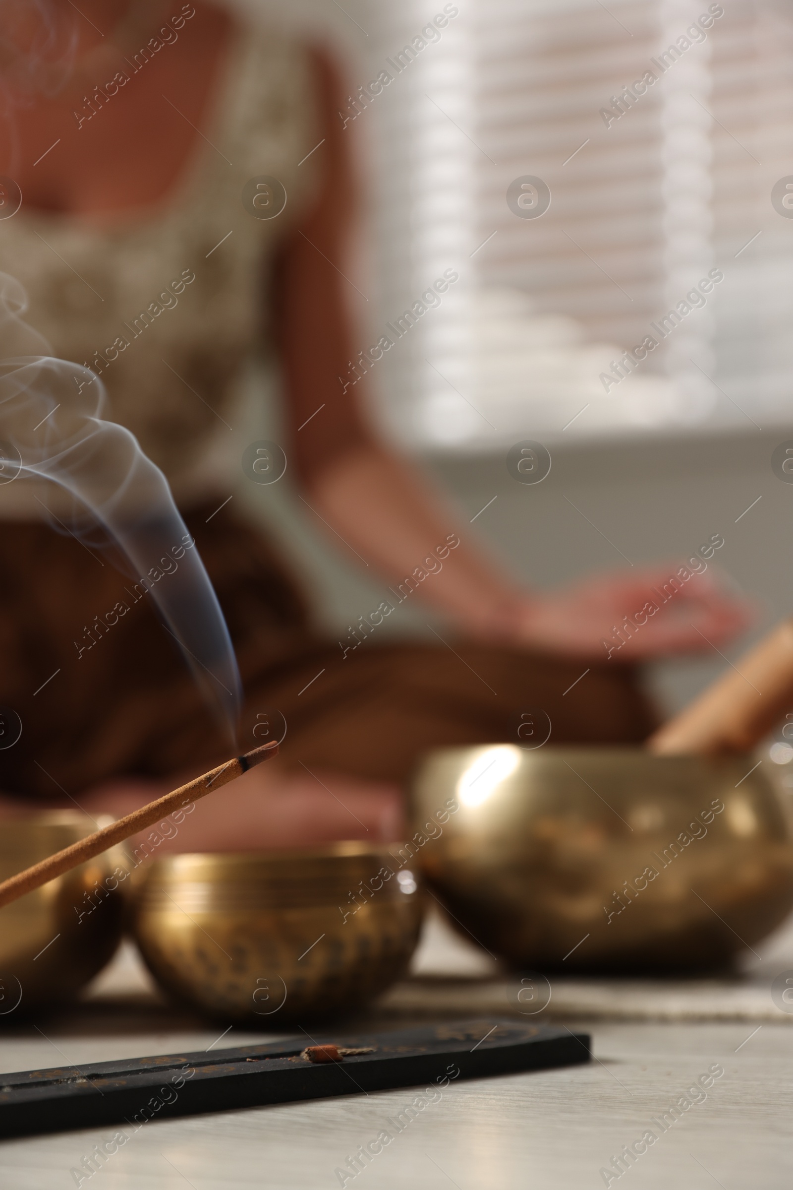 Photo of Young woman practicing yoga on floor indoors, focus on smoldering incense stick