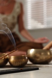 Young woman practicing yoga on floor indoors, focus on smoldering incense stick