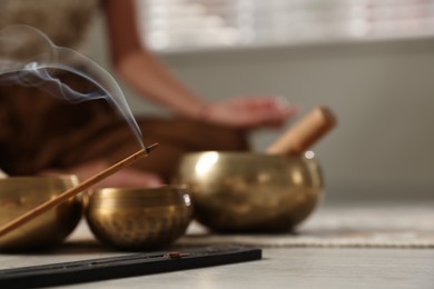 Photo of Incense stick smoldering in holder and tibetan singing bowls on floor, selective focus. Space for text