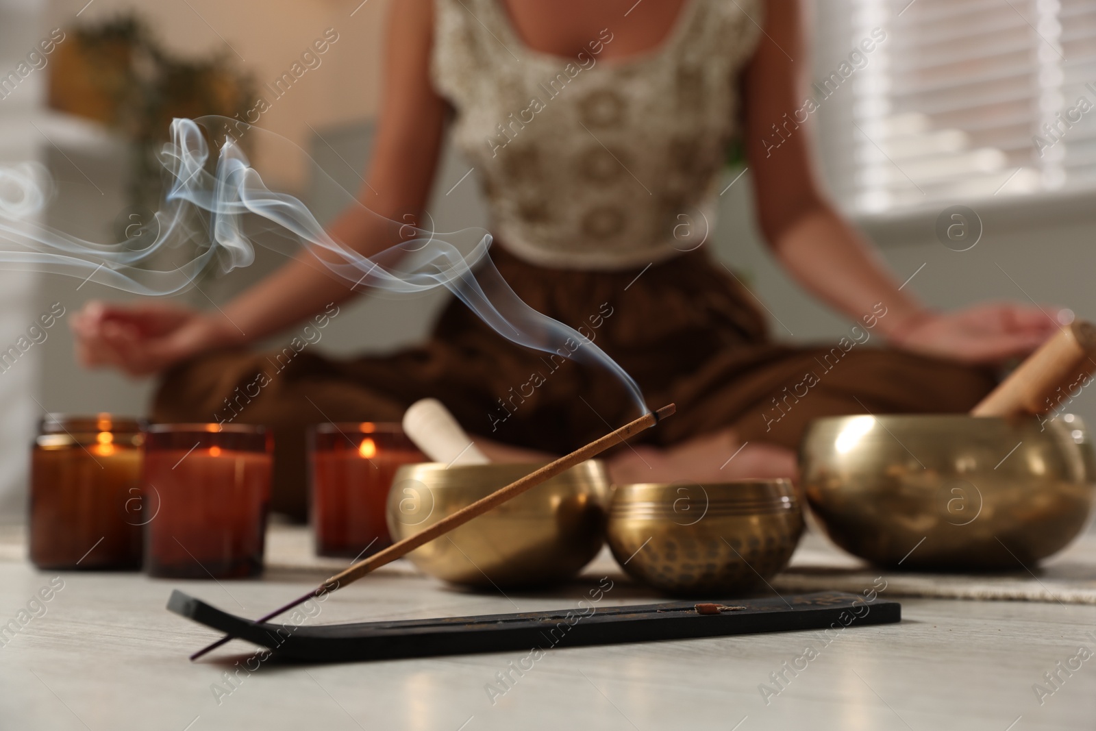 Photo of Young woman practicing yoga on floor indoors, focus on smoldering incense stick