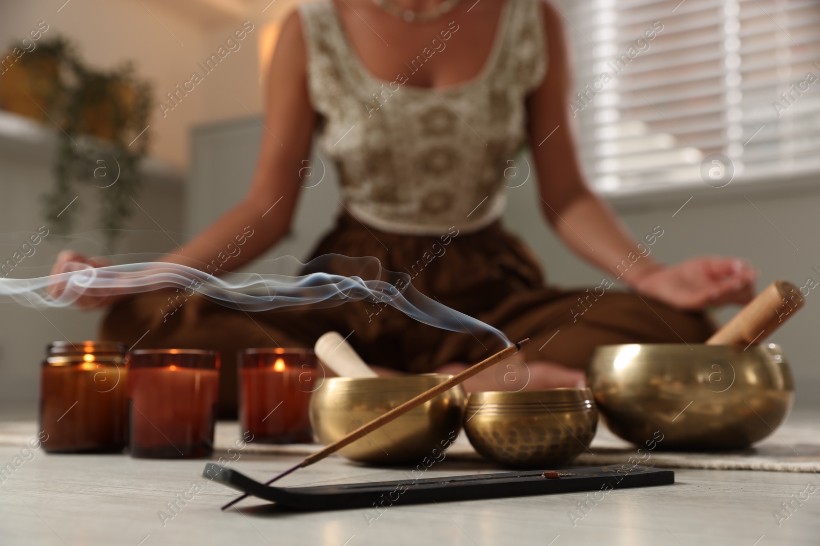 Photo of Young woman practicing yoga on floor indoors, focus on smoldering incense stick and tibetan singing bowls