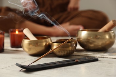 Incense stick smoldering in holder and tibetan singing bowls on floor, selective focus