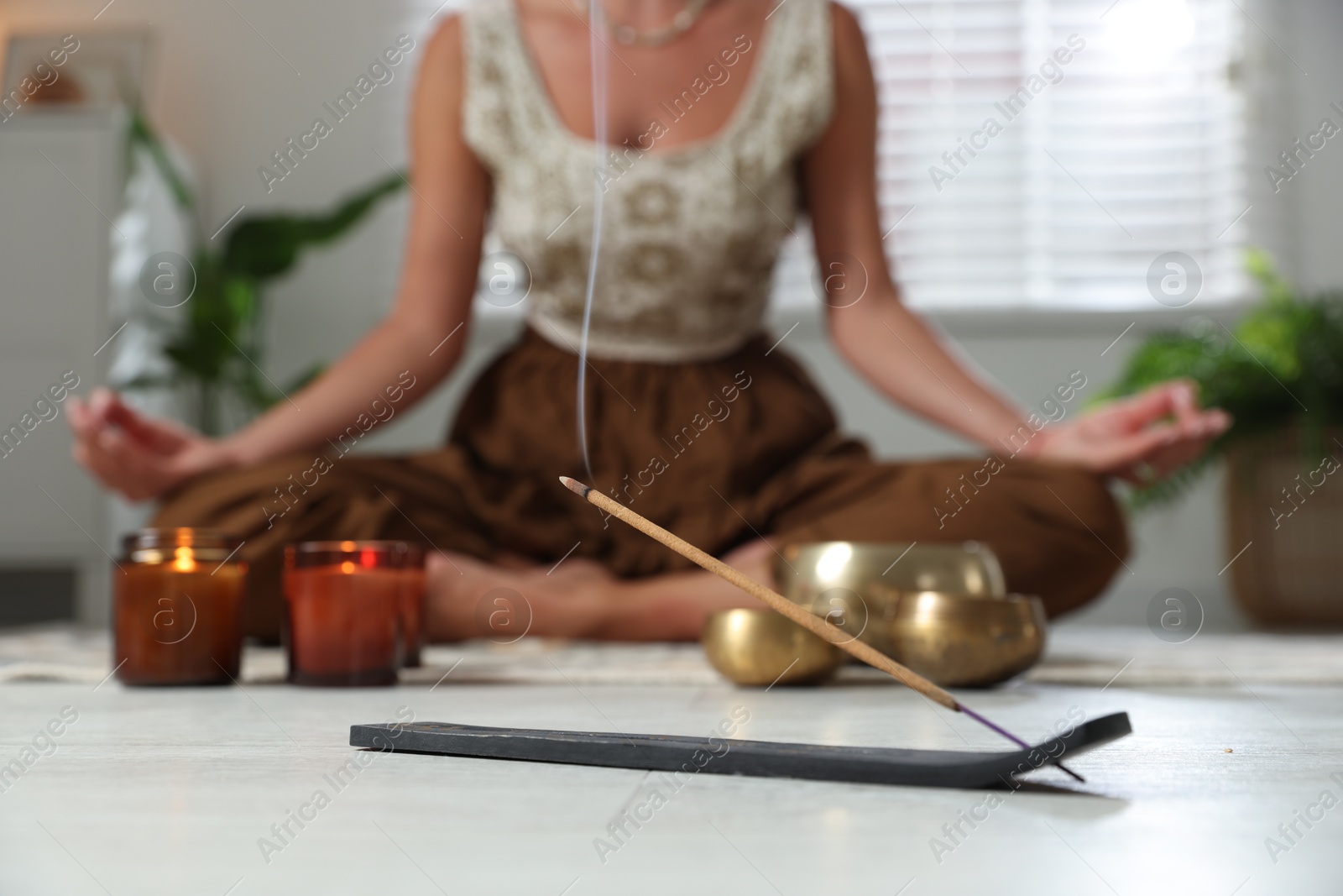 Photo of Young woman practicing yoga on floor indoors, focus on smoldering incense stick