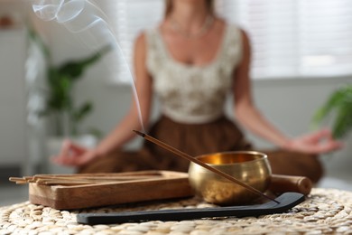 Incense stick smoldering in holder and tibetan singing bowl indoors, selective focus