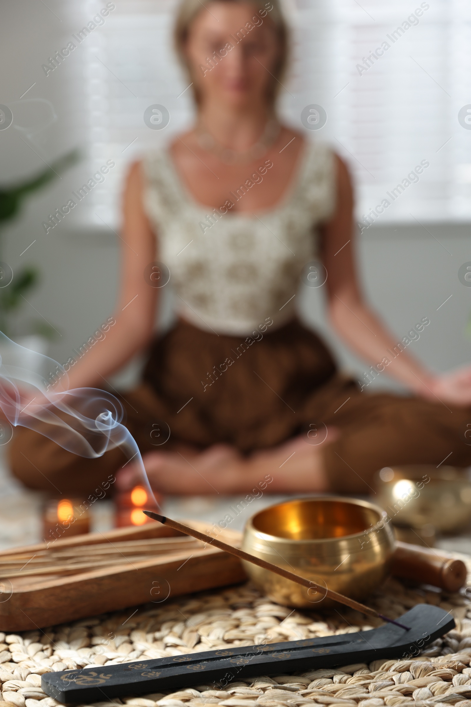 Photo of Incense stick smoldering in holder and tibetan singing bowl indoors, selective focus