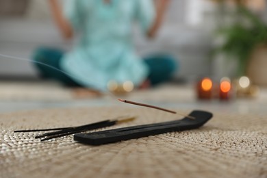 Incense stick smoldering in holder on rug indoors, selective focus