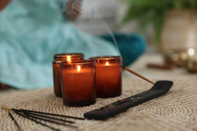 Incense sticks, holder and burning candles on wicker mat indoors, selective focus