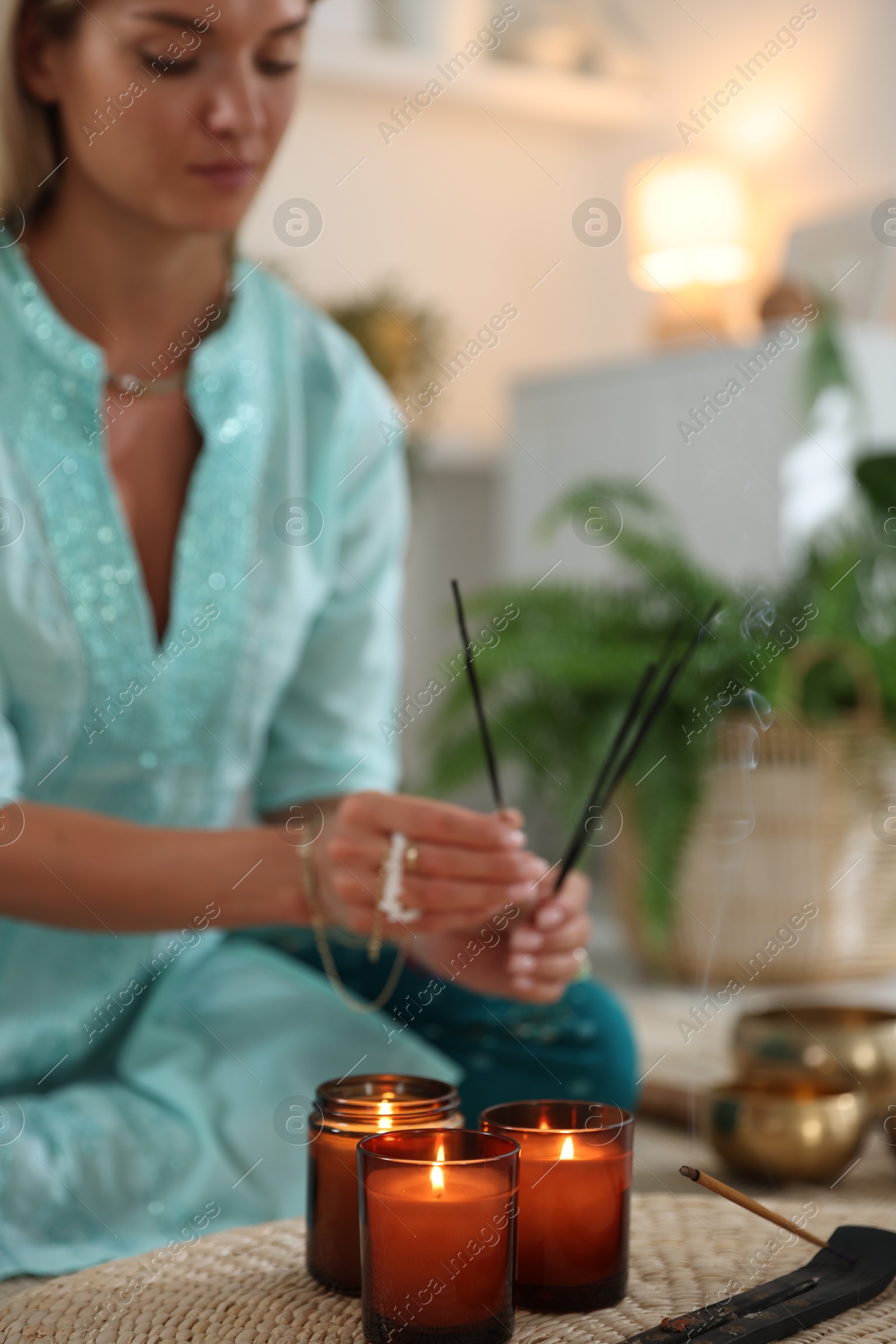 Photo of Woman with incense sticks and burning candles indoors, selective focus