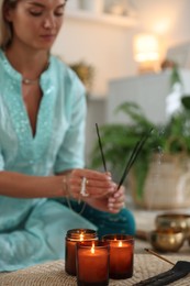 Woman with incense sticks and burning candles indoors, selective focus