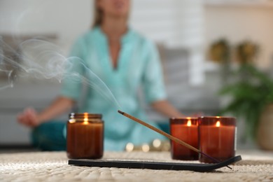 Incense stick smoldering in holder and burning candles on wicker mat indoors, selective focus