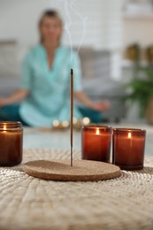 Photo of Incense stick smoldering in holder and burning candles on wicker mat indoors, selective focus