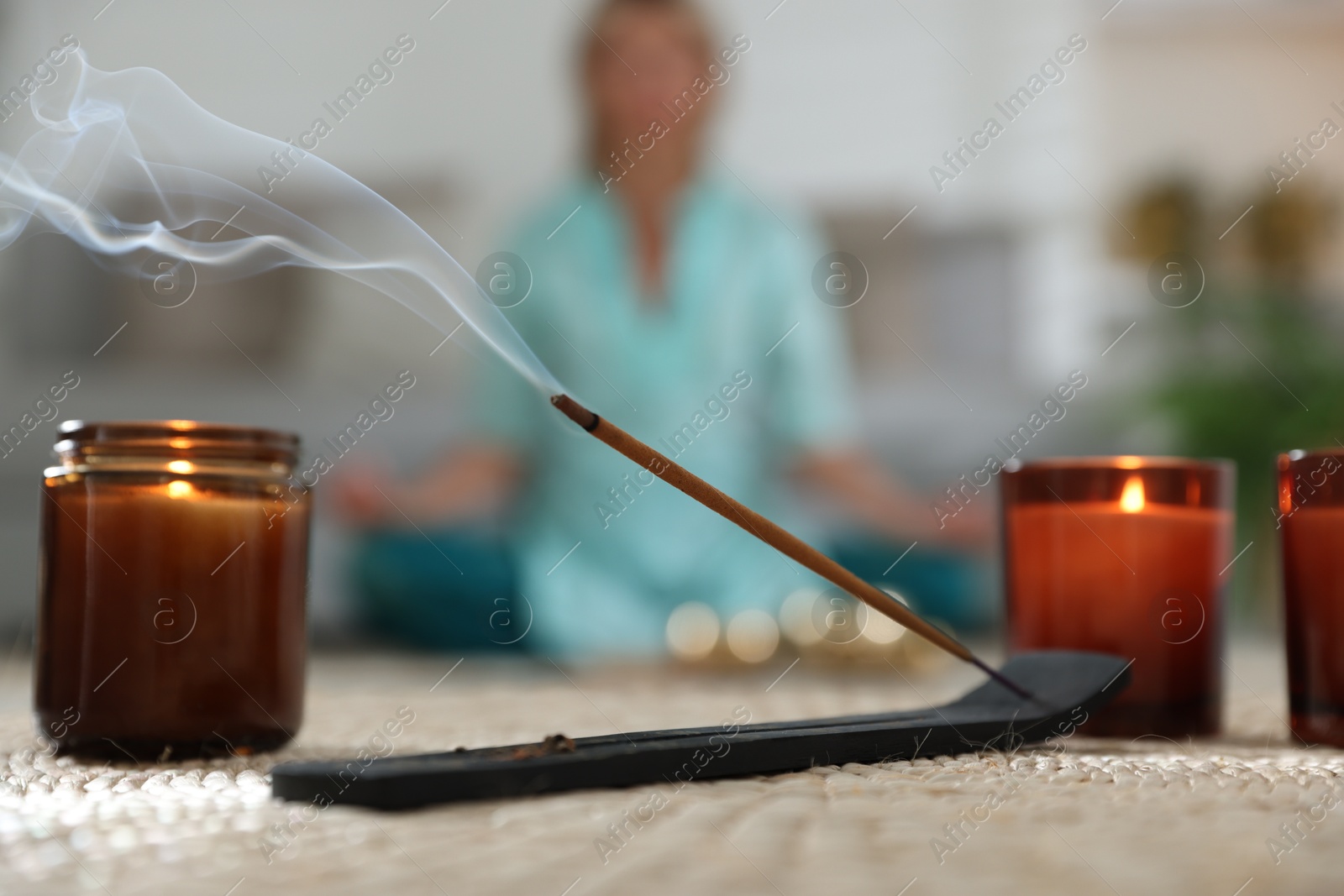 Photo of Incense stick smoldering in holder and burning candles on wicker mat indoors, selective focus