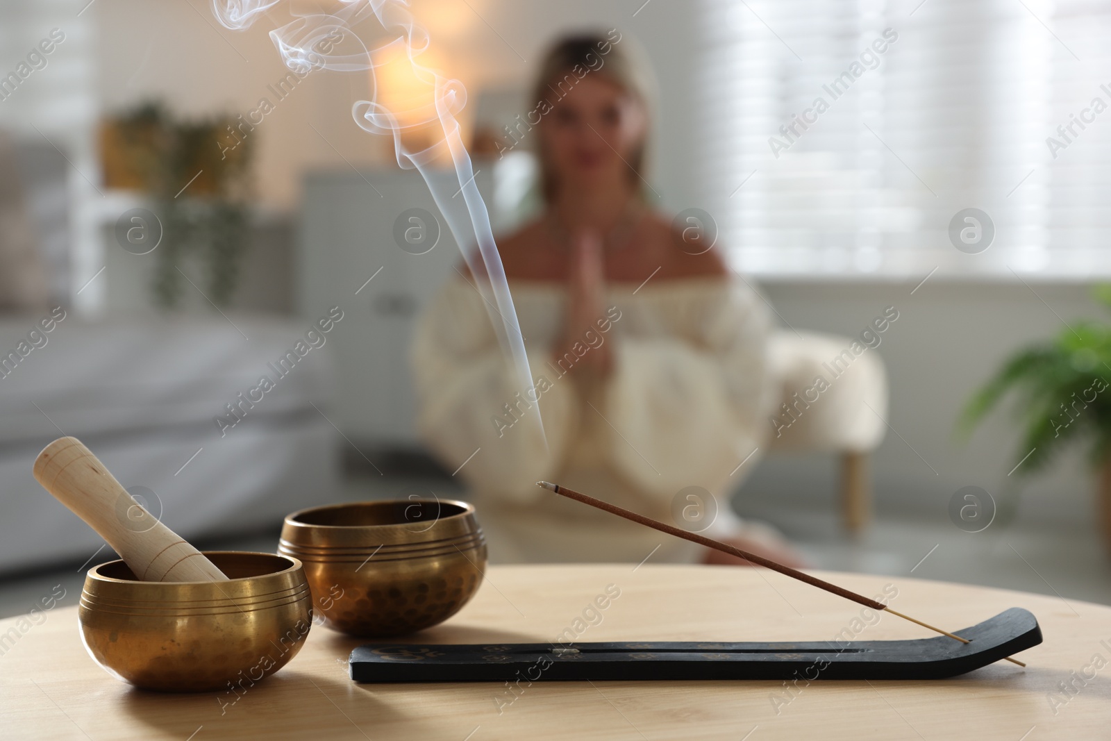 Photo of Incense stick smoldering in holder and tibetan singing bowls on wooden table indoors, selective focus