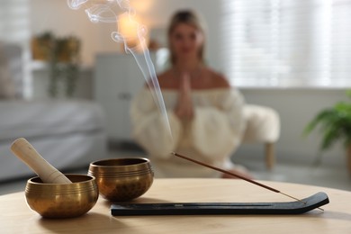 Incense stick smoldering in holder and tibetan singing bowls on wooden table indoors, selective focus