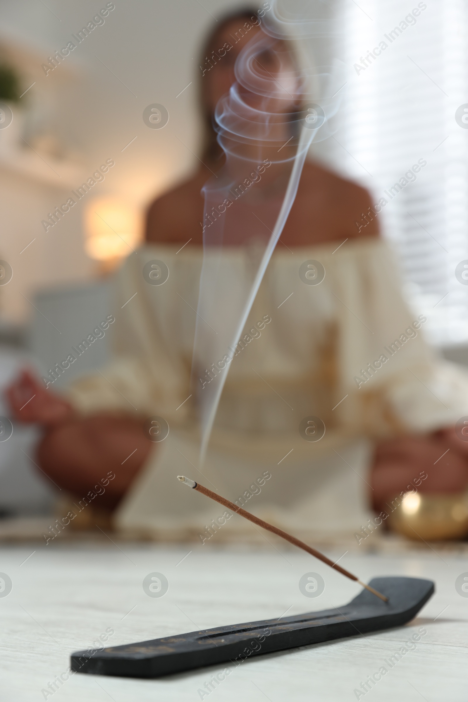 Photo of Incense stick smoldering in holder on floor indoors, selective focus