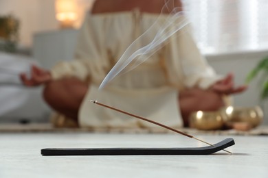 Incense stick smoldering in holder on floor indoors, selective focus