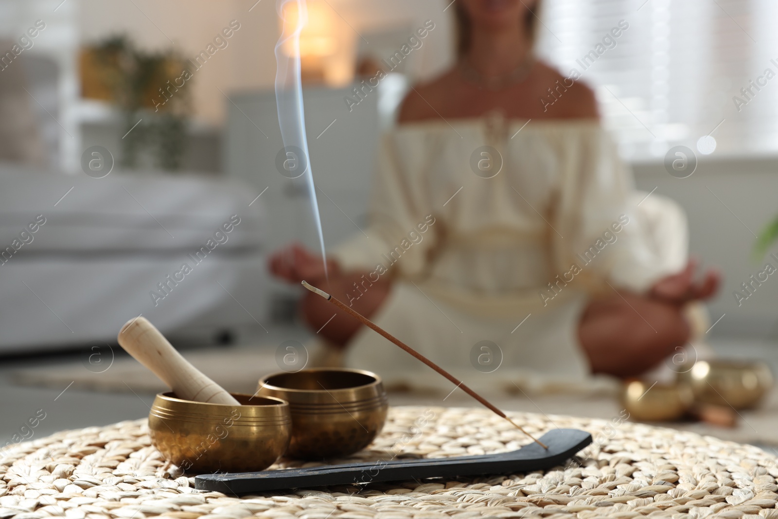 Photo of Young woman practicing yoga on floor indoors, focus on smoldering incense stick and tibetan singing bowls