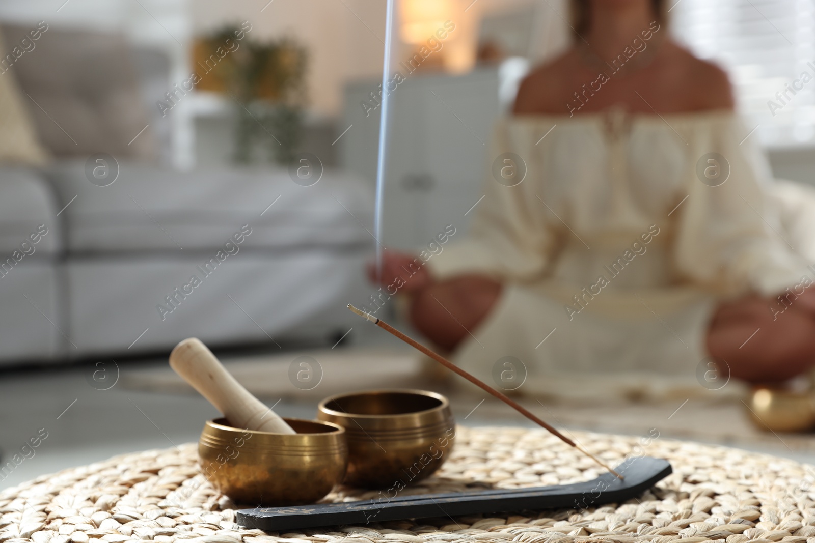 Photo of Young woman practicing yoga on floor indoors, focus on smoldering incense stick and tibetan singing bowls