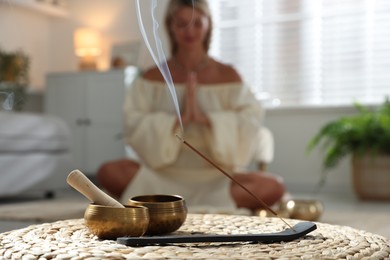 Young woman practicing yoga on floor indoors, focus on smoldering incense stick and tibetan singing bowls