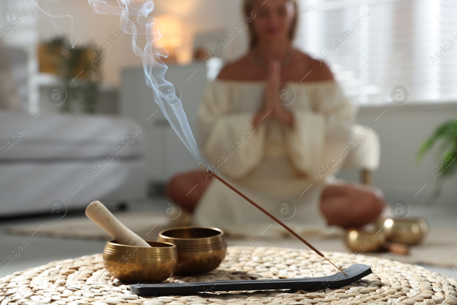 Photo of Young woman practicing yoga on floor indoors, focus on smoldering incense stick and tibetan singing bowls