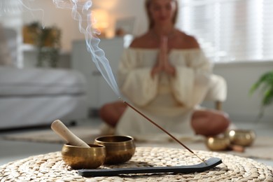 Young woman practicing yoga on floor indoors, focus on smoldering incense stick and tibetan singing bowls