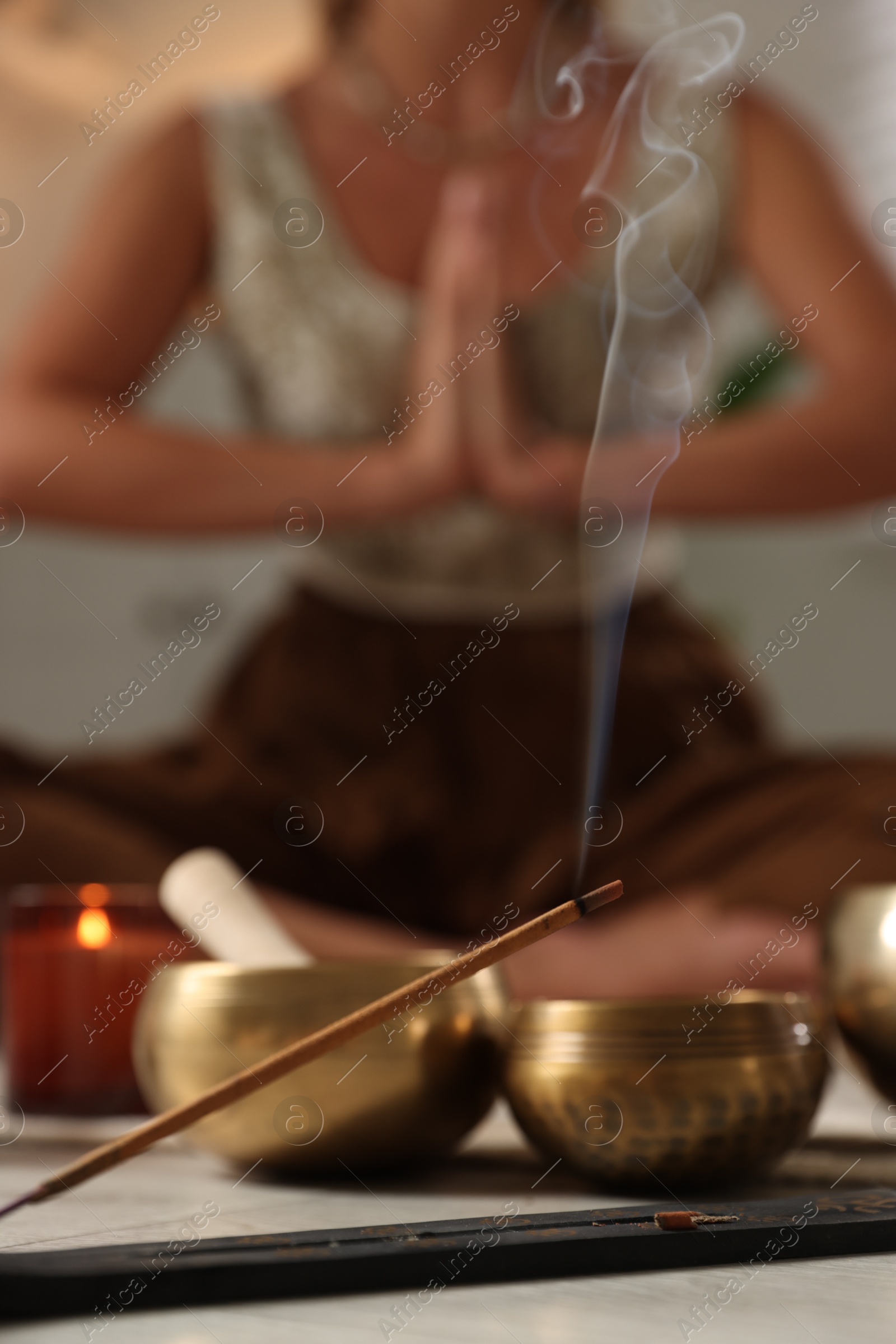 Photo of Young woman practicing yoga indoors, focus on smoldering incense stick and tibetan singing bowls