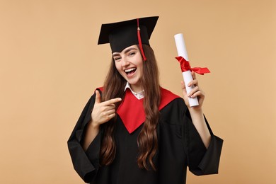 Photo of Happy student pointing at diploma after graduation on beige background