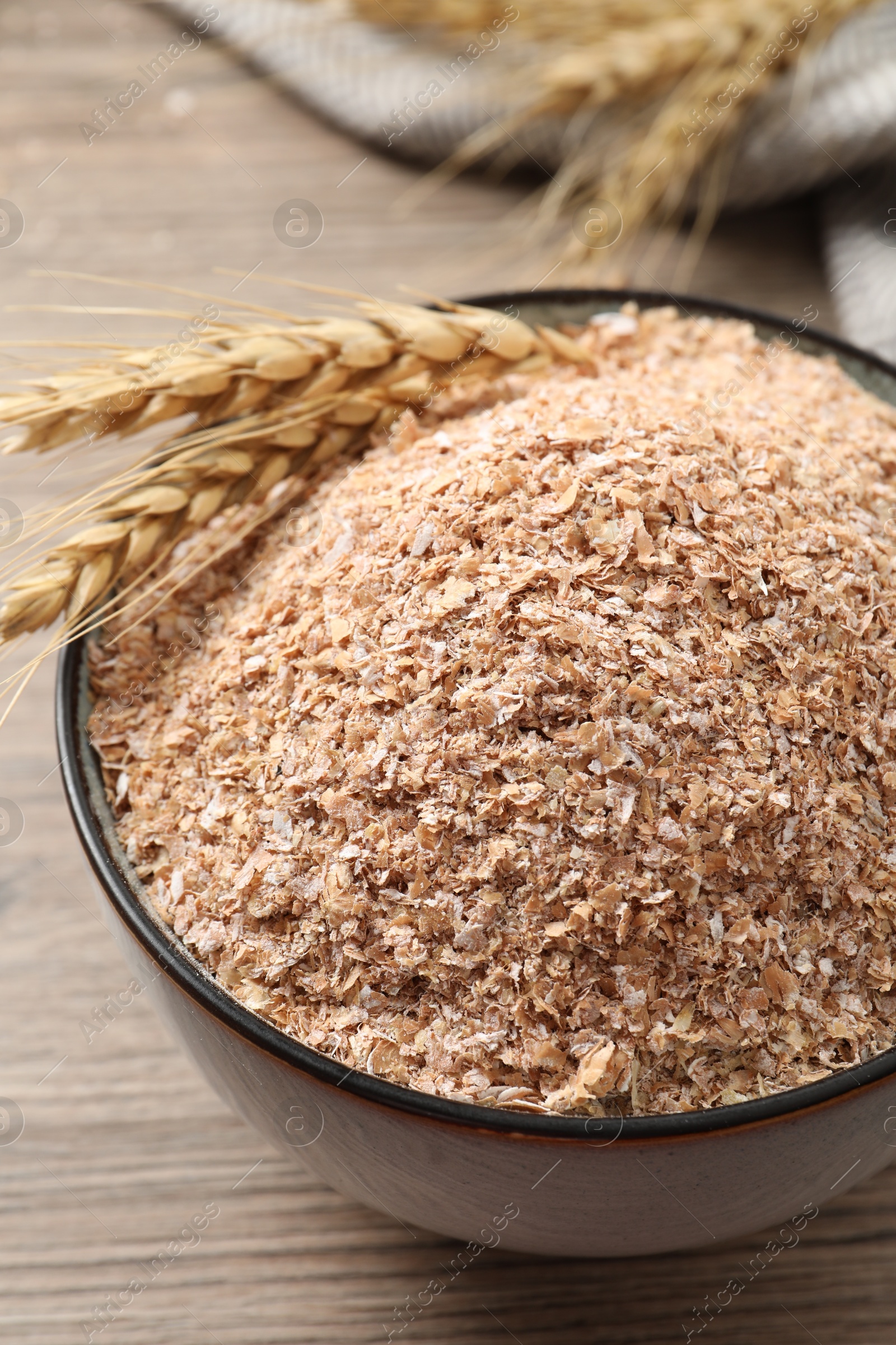 Photo of Wheat bran and spikelets in bowl on wooden table