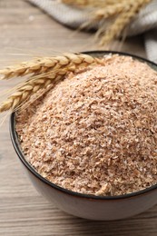 Wheat bran and spikelets in bowl on wooden table