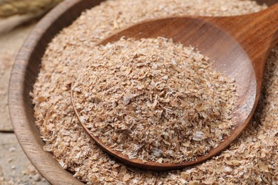 Photo of Wheat bran and spoon in bowl on table, closeup