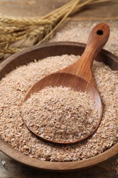 Wheat bran and spoon in bowl on wooden table