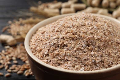 Photo of Bowl of wheat bran on black table, closeup