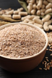 Photo of Bowl of wheat bran on black wooden table