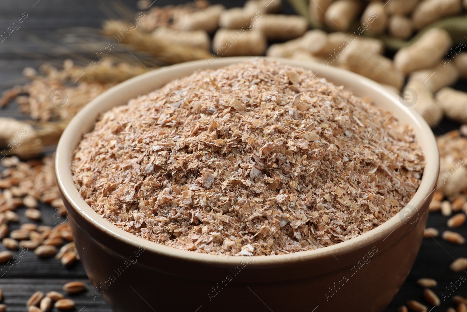 Photo of Bowl of wheat bran on black table, closeup