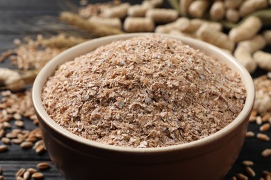 Bowl of wheat bran on black table, closeup