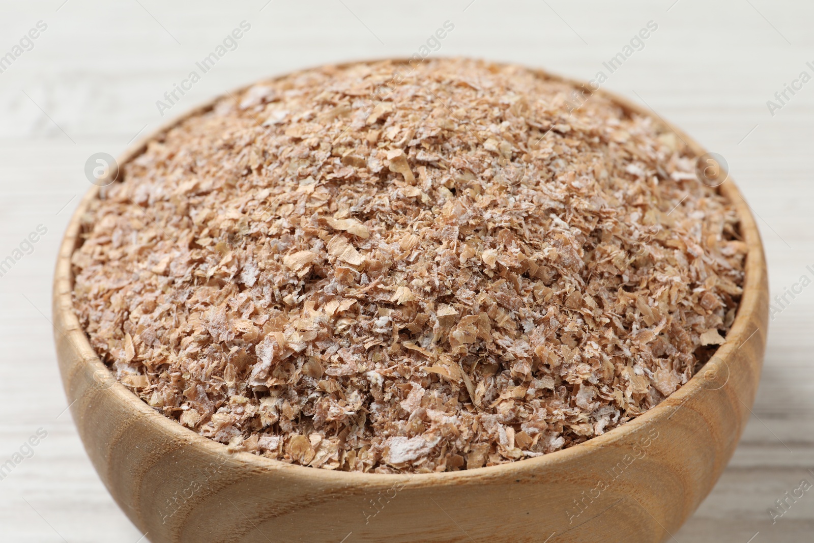 Photo of Bowl of wheat bran on white wooden table, closeup