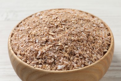 Bowl of wheat bran on white wooden table, closeup