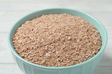 Photo of Bowl of wheat bran on white wooden table, closeup