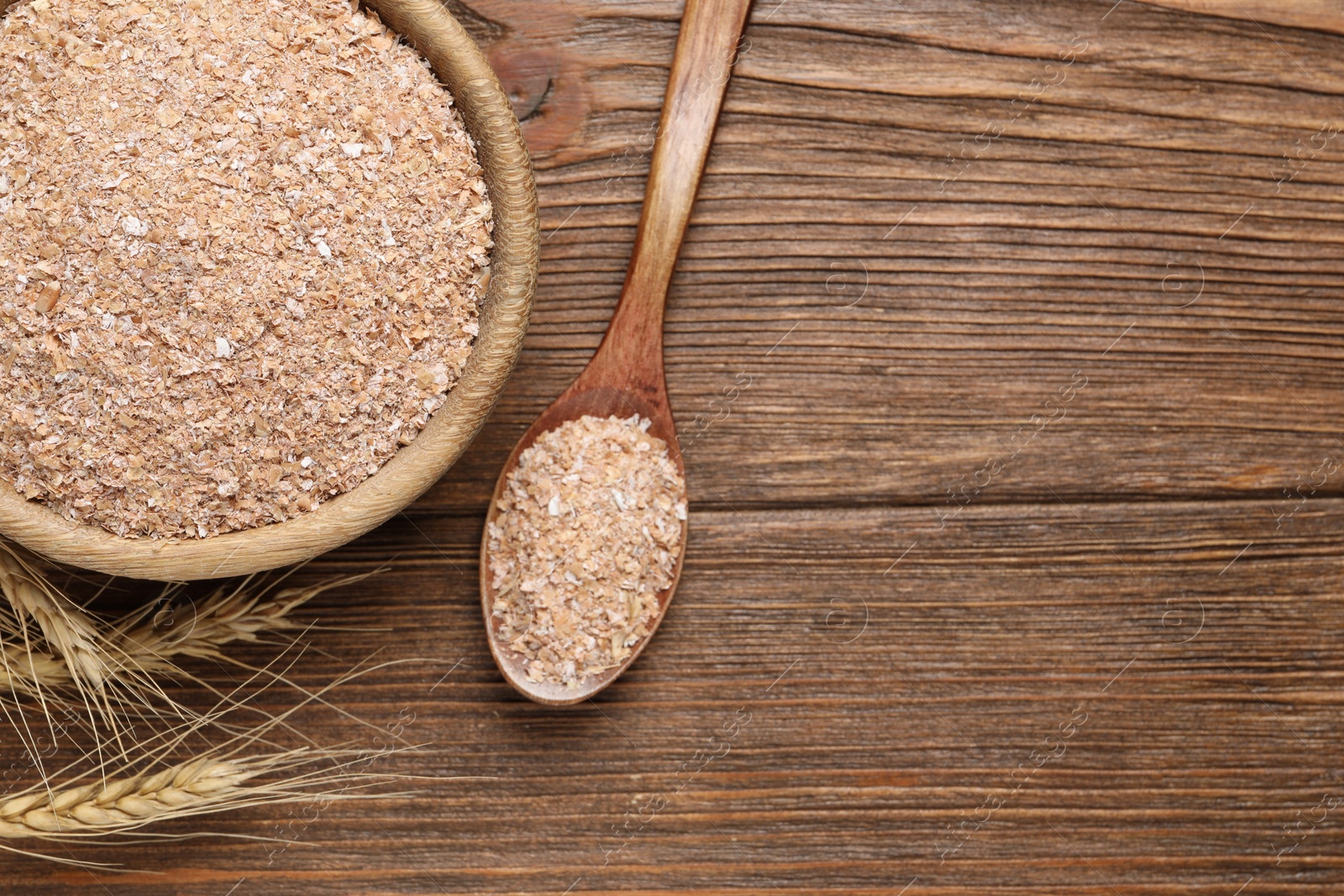 Photo of Spoon and bowl with wheat bran on wooden table, flat lay. Space for text