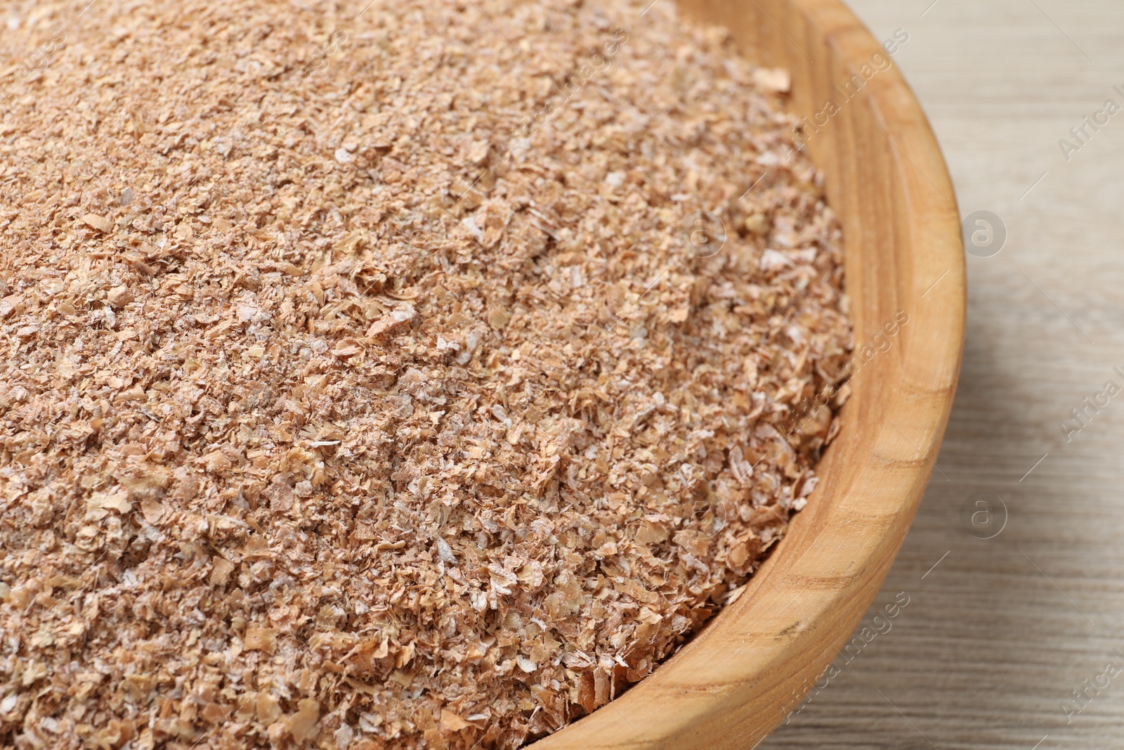 Photo of Bowl of wheat bran on white wooden table, closeup