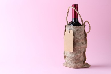 Photo of Wine bottle in burlap bag on pink background. Space for text