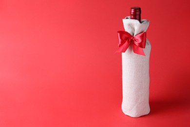 Photo of Wine bottle in burlap bag with satin bow on red background. Space for text