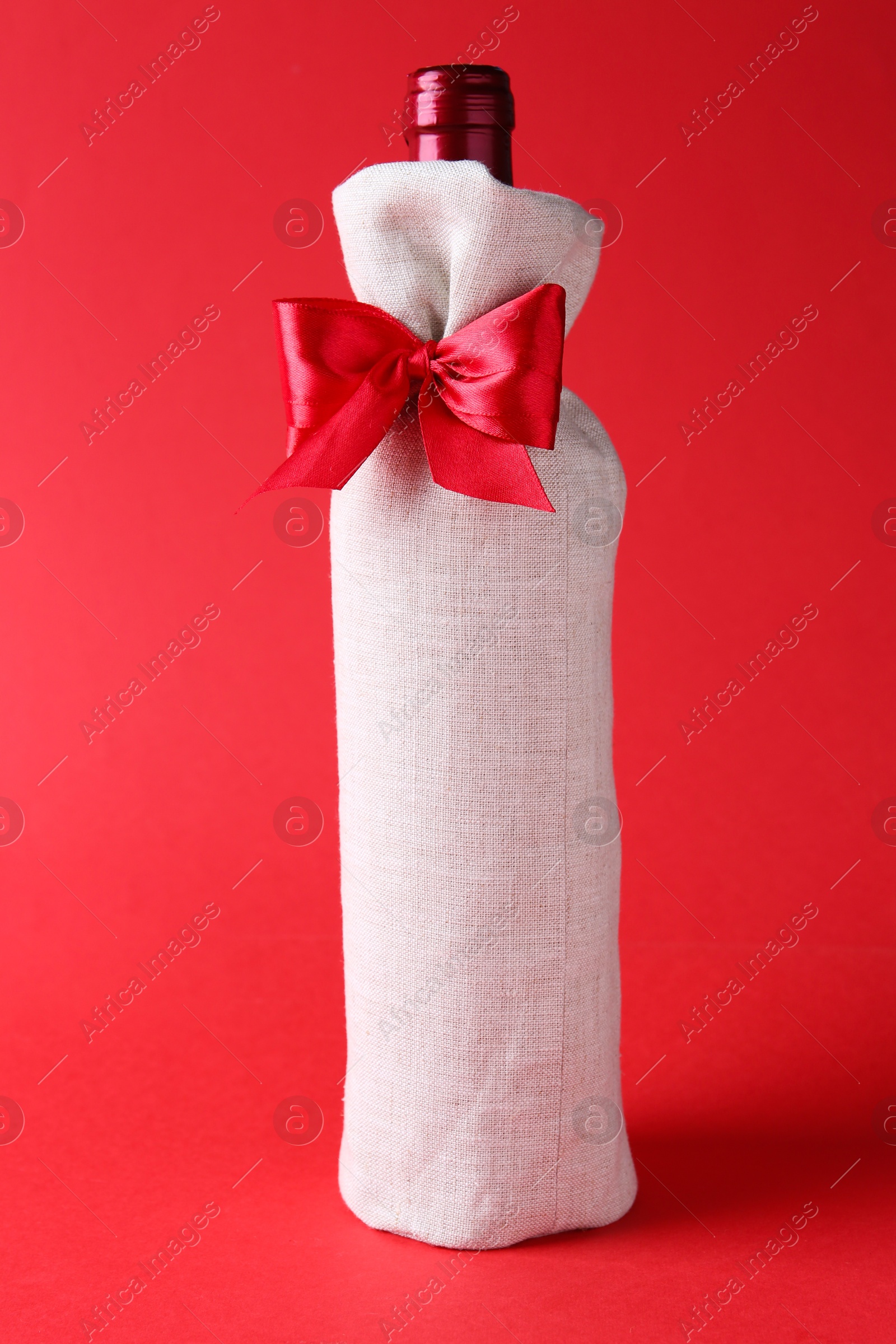 Photo of Wine bottle in burlap bag with satin bow on red background