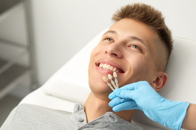 Doctor checking young man's teeth color in clinic, closeup. Dental veneers