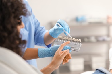 Doctor and patient choosing shade on teeth color palette in clinic, closeup. Dental veneers