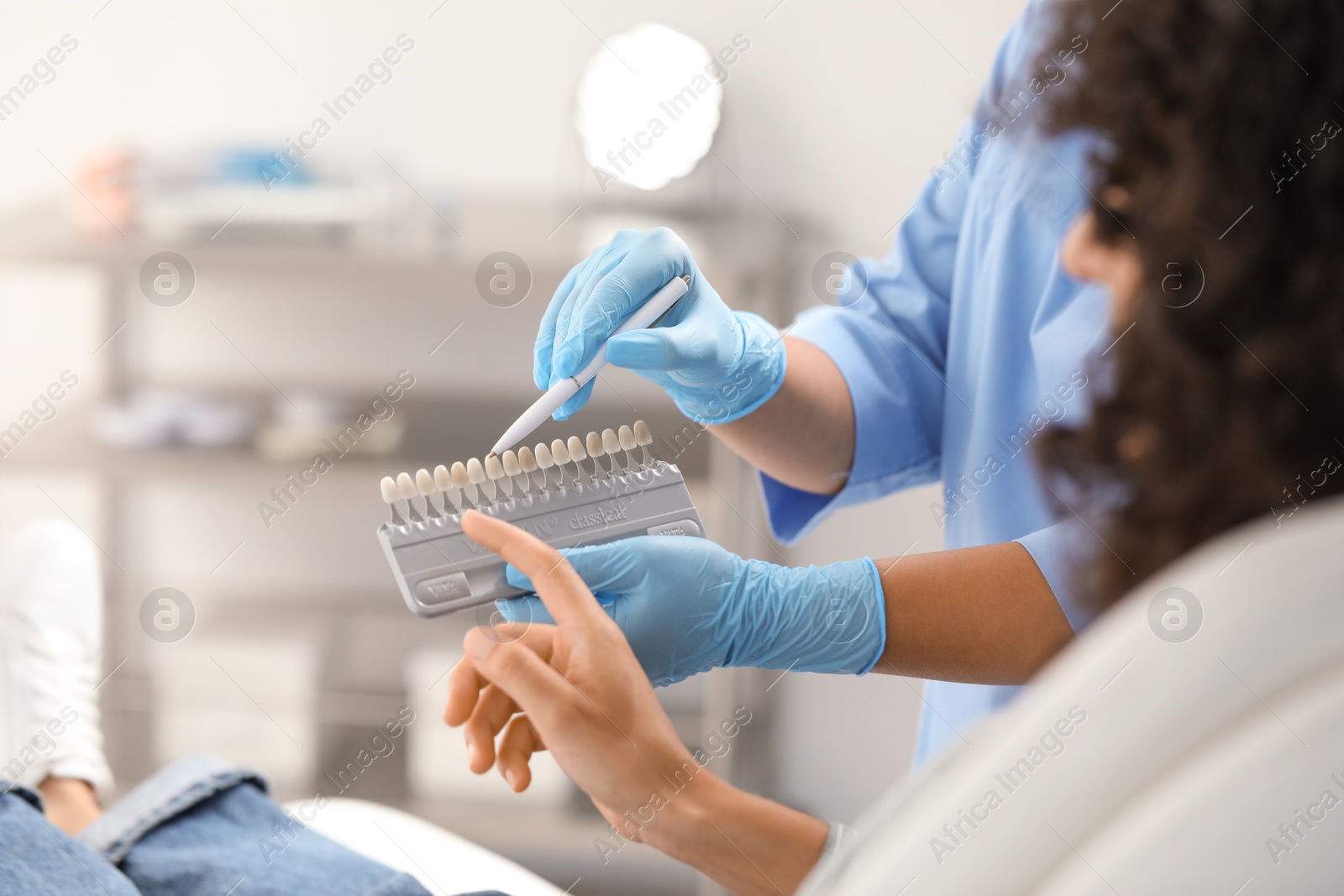 Photo of Doctor and patient choosing shade on teeth color palette in clinic, closeup. Dental veneers