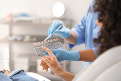 Doctor and patient choosing shade on teeth color palette in clinic, closeup. Dental veneers